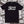 Load image into Gallery viewer, A black Almost Official glitch logo shirt on a poster background.