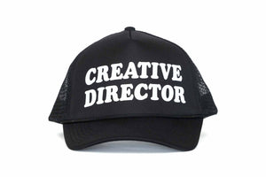 The front of a black trucker hat with the text Creative Director printed in white.