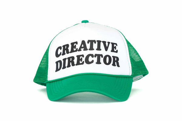 The front of a green and white trucker hat with the text Creative Director printed in black. 