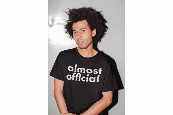 A man wearing the Almost Official Glitch Logo black t-shirt