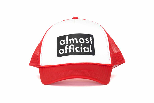 The front of a red and white trucker hat with the Almost Official black stamp logo printed on the front panel. 