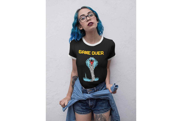 A cool young woman wearing the retro ringer Cobra Boss tee that depicts a colorful 8 bit cobra and the words Game Over.